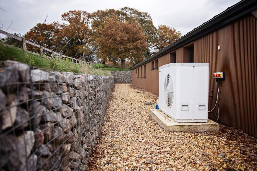 Air source heat pump on a gravel path beside a timber-clad building