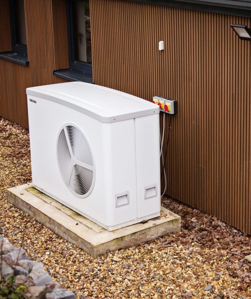 Air source heat pump on a raised base beside a timber wall