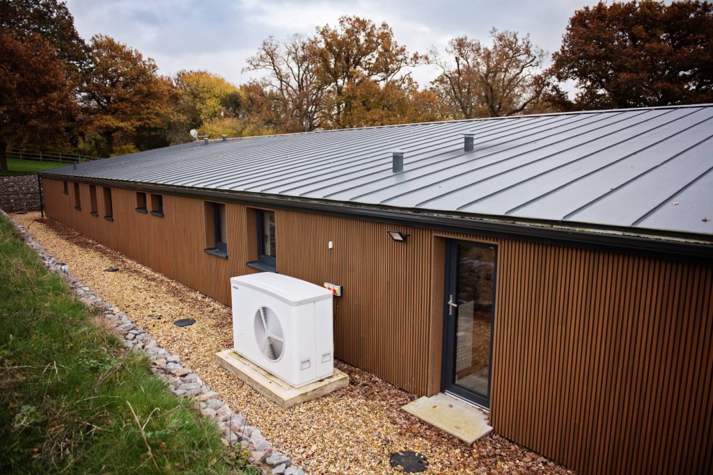 Air source heat pump beside a long timber-clad building