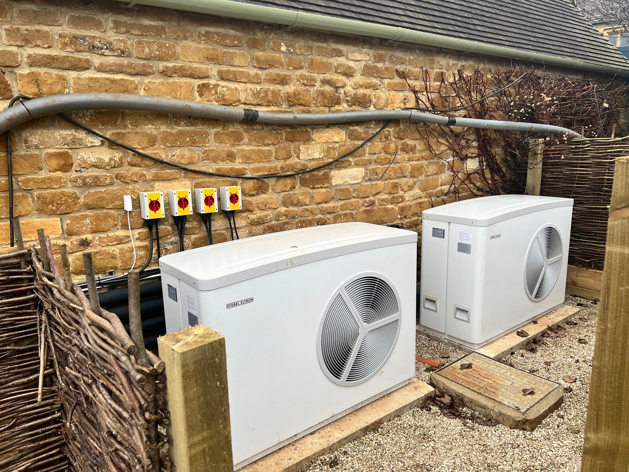 Two air source heat pumps installed beside a stone wall