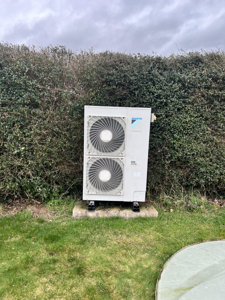 Air source heat pump on a lawn in front of a hedge