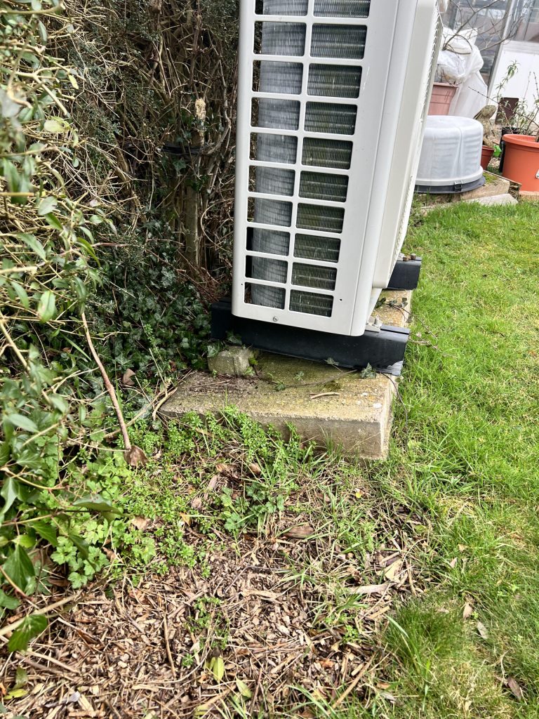 Air source heat pump on grass beside a hedge
