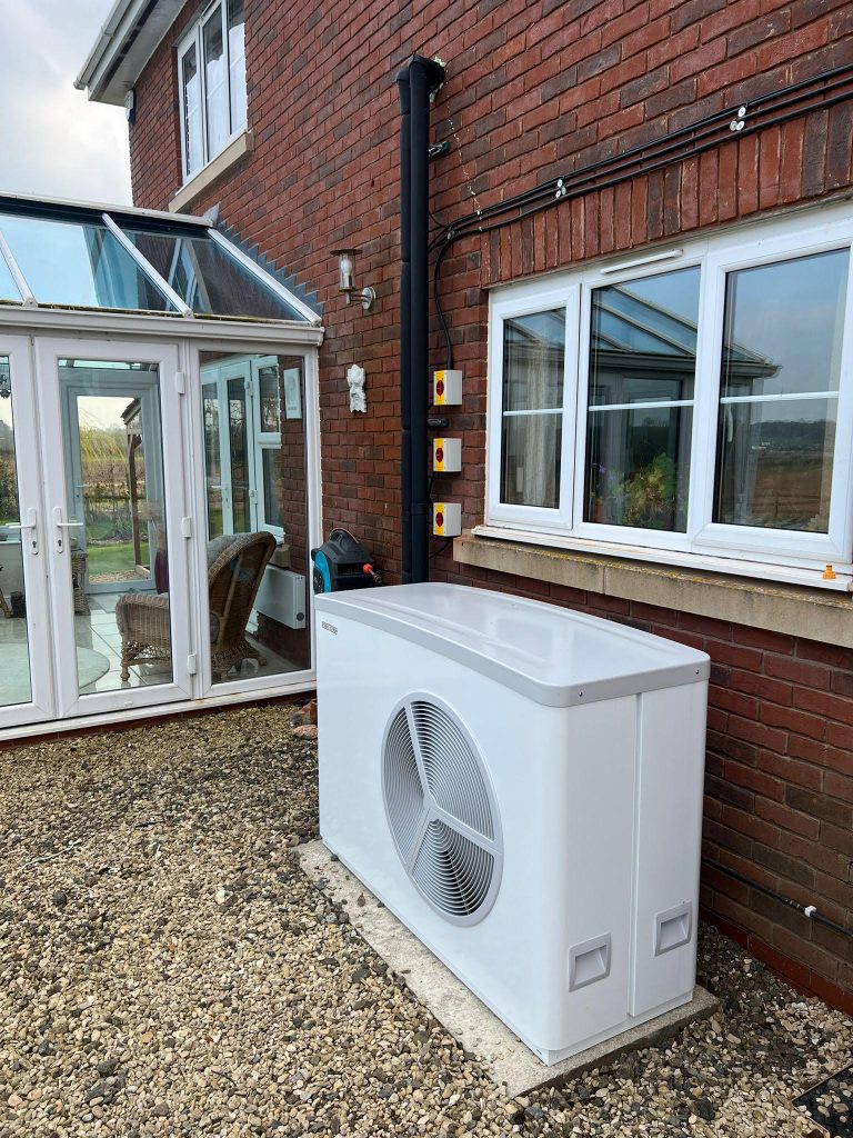 Air source heat pump on gravel beside a conservatory