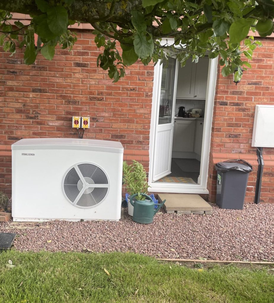 Air source heat pump beside the back door of a brick house